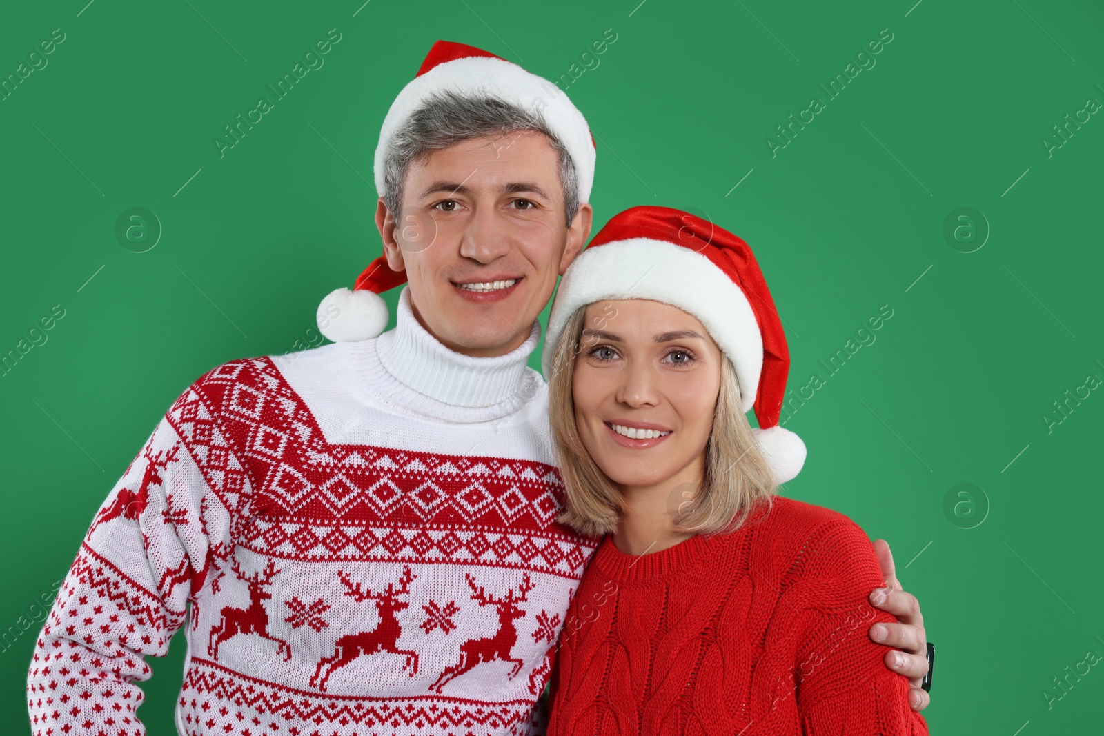 Photo of Happy couple in Christmas sweaters and Santa hats on green background