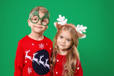 Photo of Cute little children in Christmas sweaters and accessories on green background