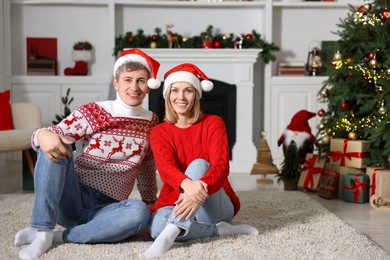 Lovely couple in Christmas sweaters and Santa hats at home