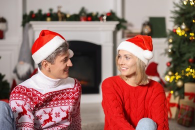 Photo of Lovely couple in Christmas sweaters and Santa hats at home