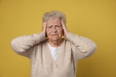 Photo of Senior woman covering her ears on dark yellow background