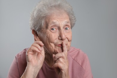 Photo of Senior woman showing hand to ear gesture on grey background