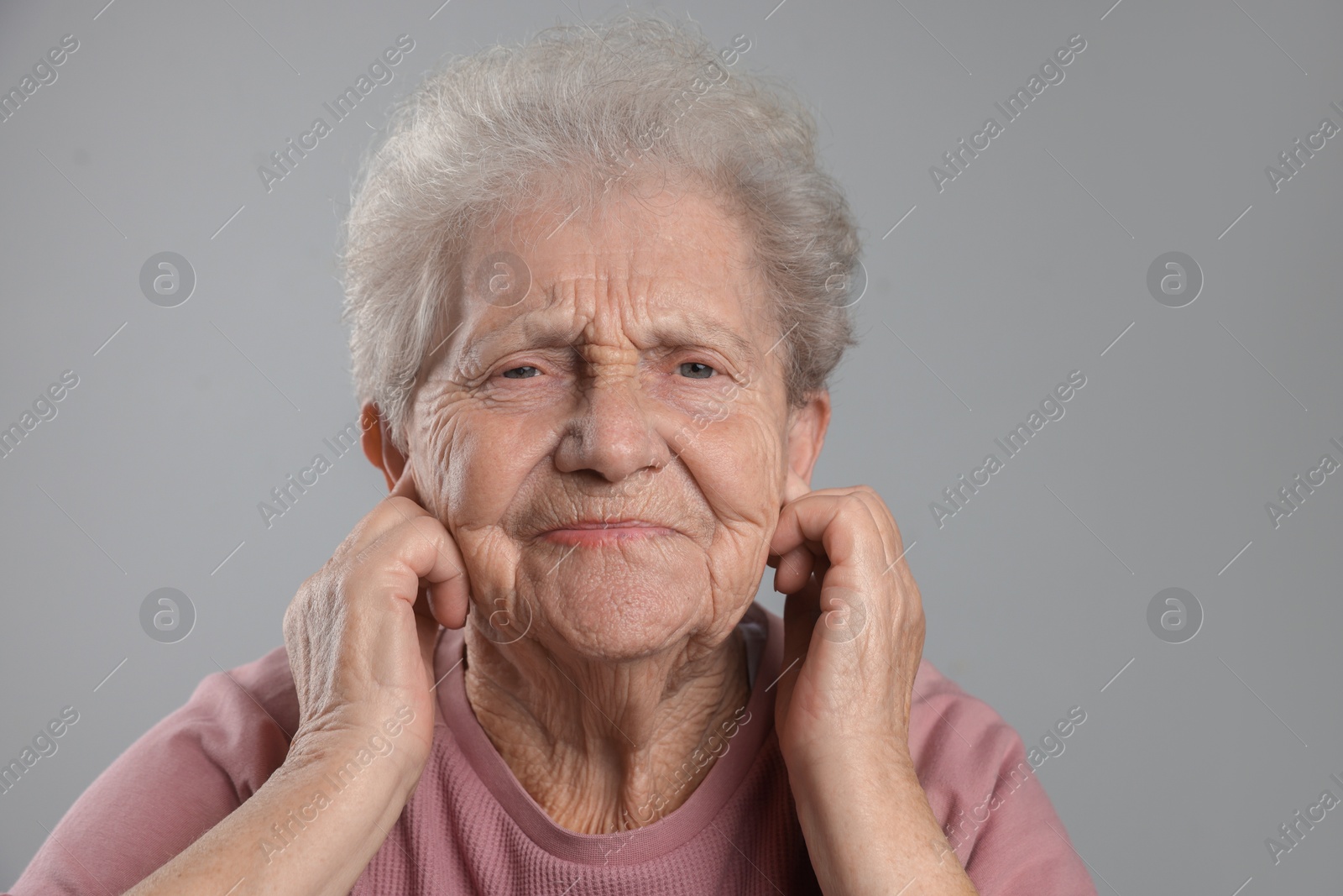 Photo of Senior woman covering her ears with fingers on grey background