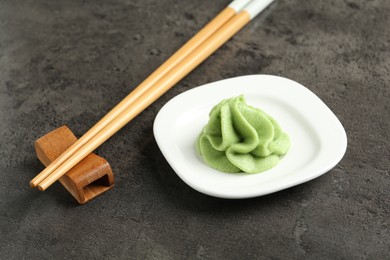 Photo of Hot wasabi paste and chopsticks on grey textured table, closeup