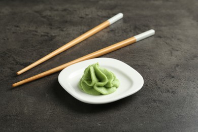 Photo of Hot wasabi paste and chopsticks on grey textured table, closeup