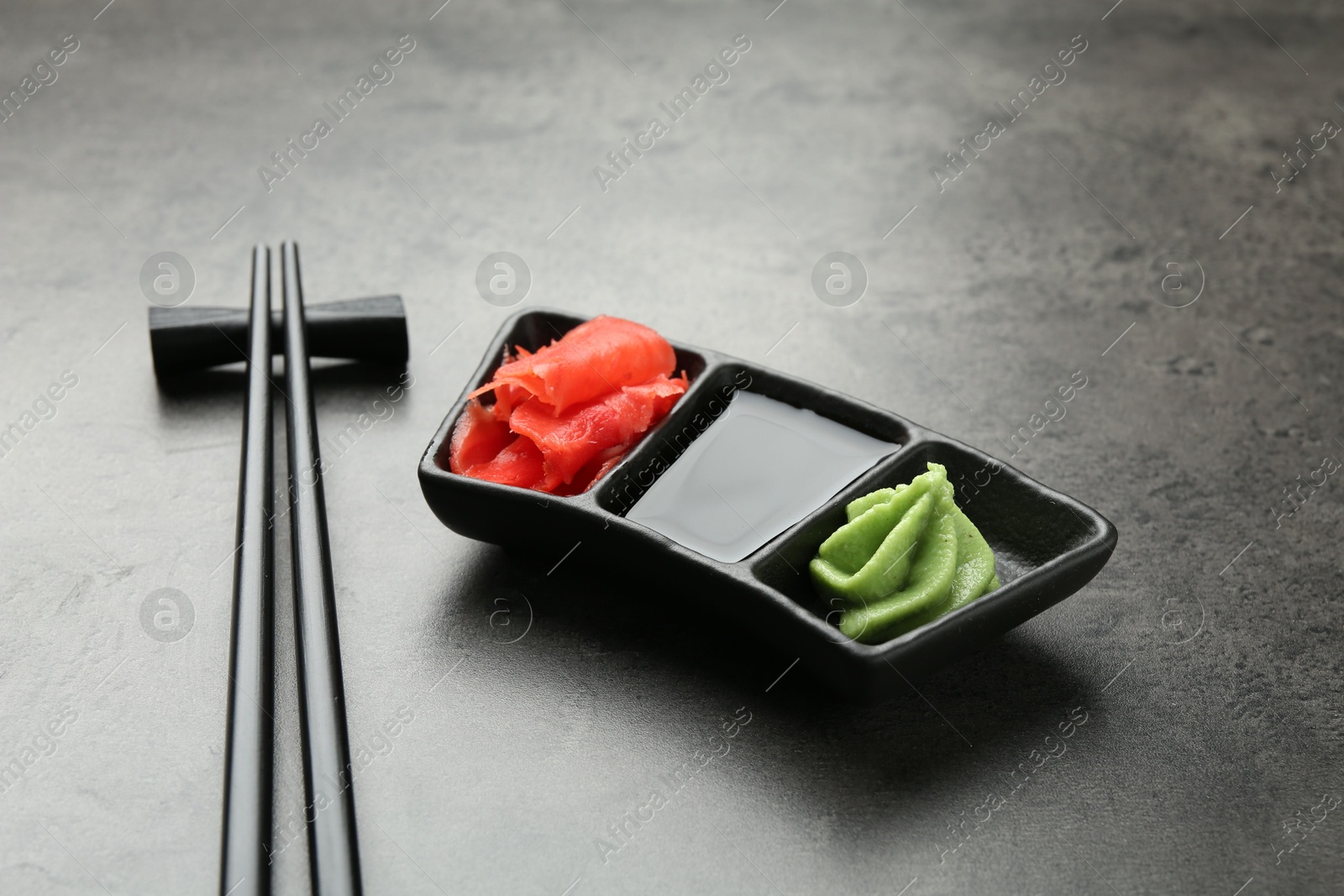 Photo of Hot wasabi paste, soy sauce, ginger and chopsticks on grey textured table, closeup