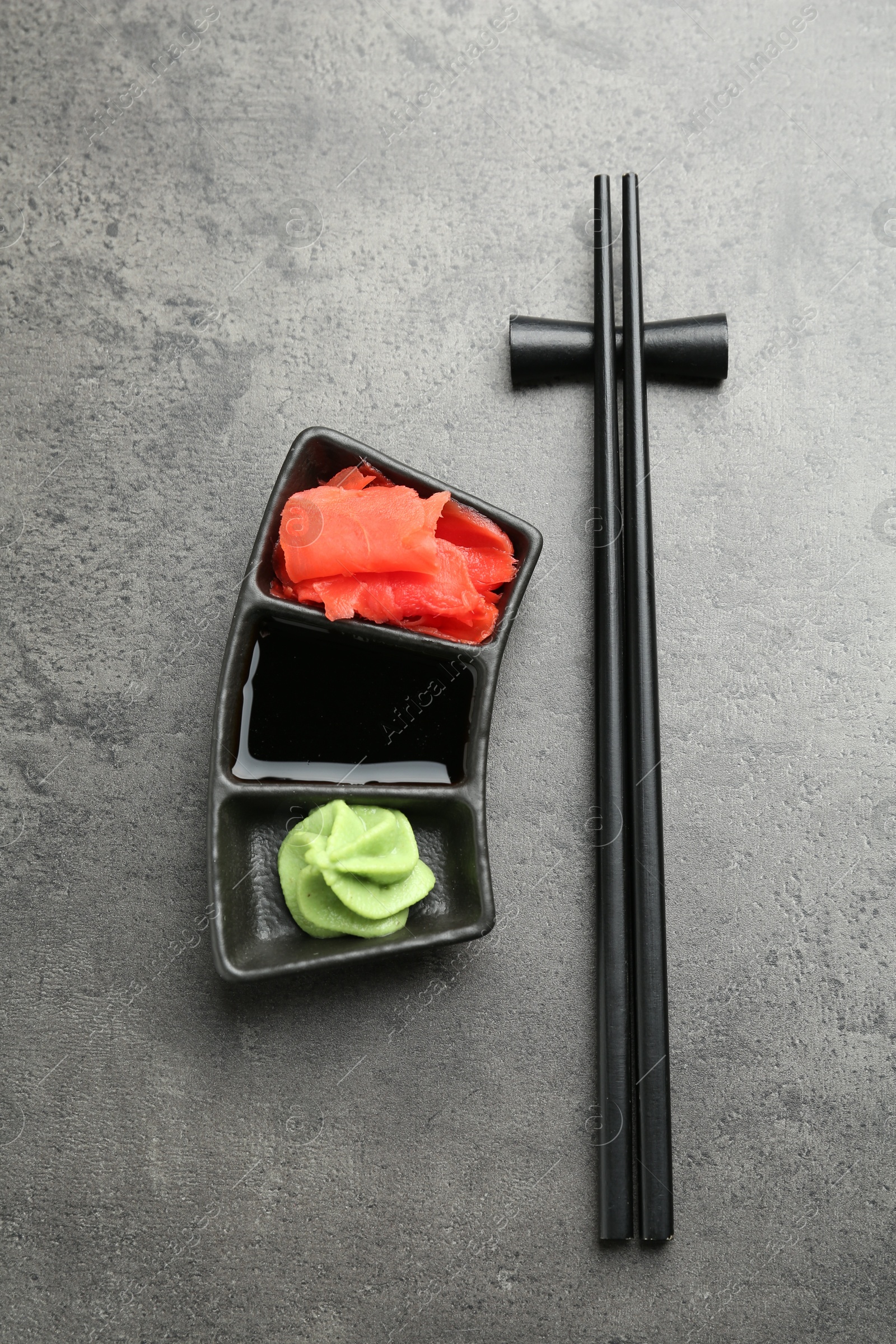 Photo of Hot wasabi paste, soy sauce, ginger and chopsticks on grey textured table, top view