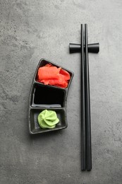 Photo of Hot wasabi paste, soy sauce, ginger and chopsticks on grey textured table, top view