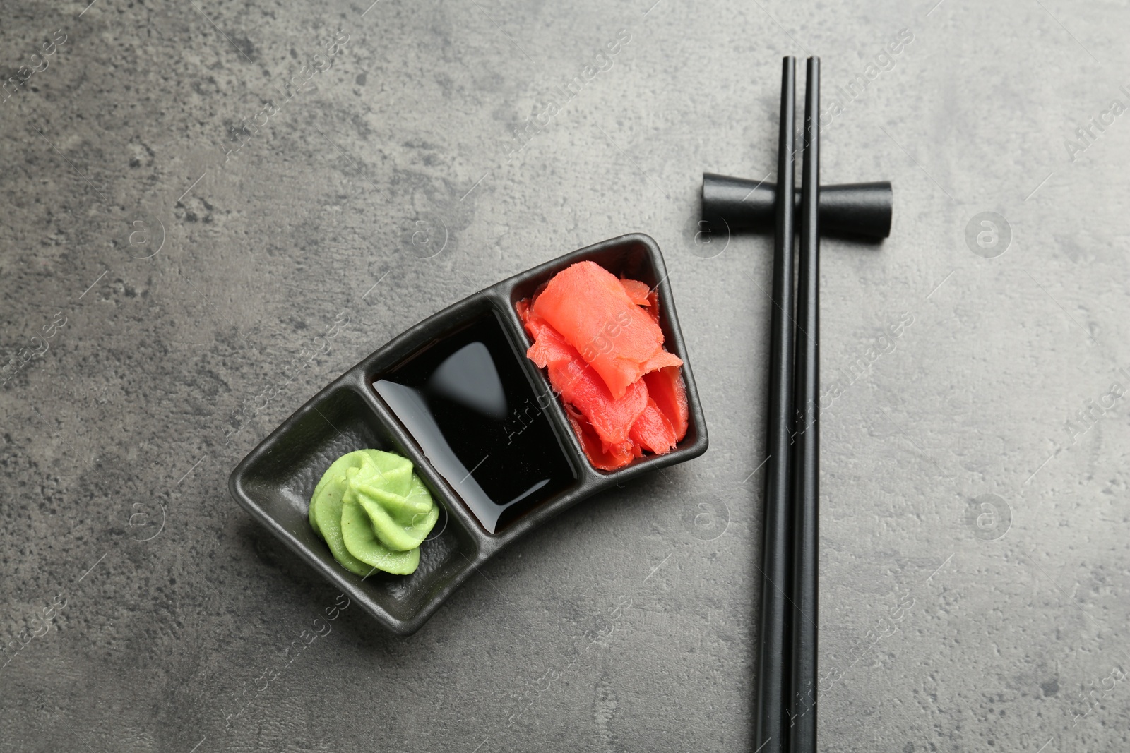 Photo of Hot wasabi paste, soy sauce, ginger and chopsticks on grey textured table, top view