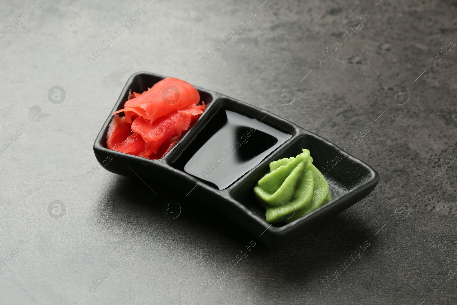 Photo of Hot wasabi paste, soy sauce and ginger on grey textured table, closeup