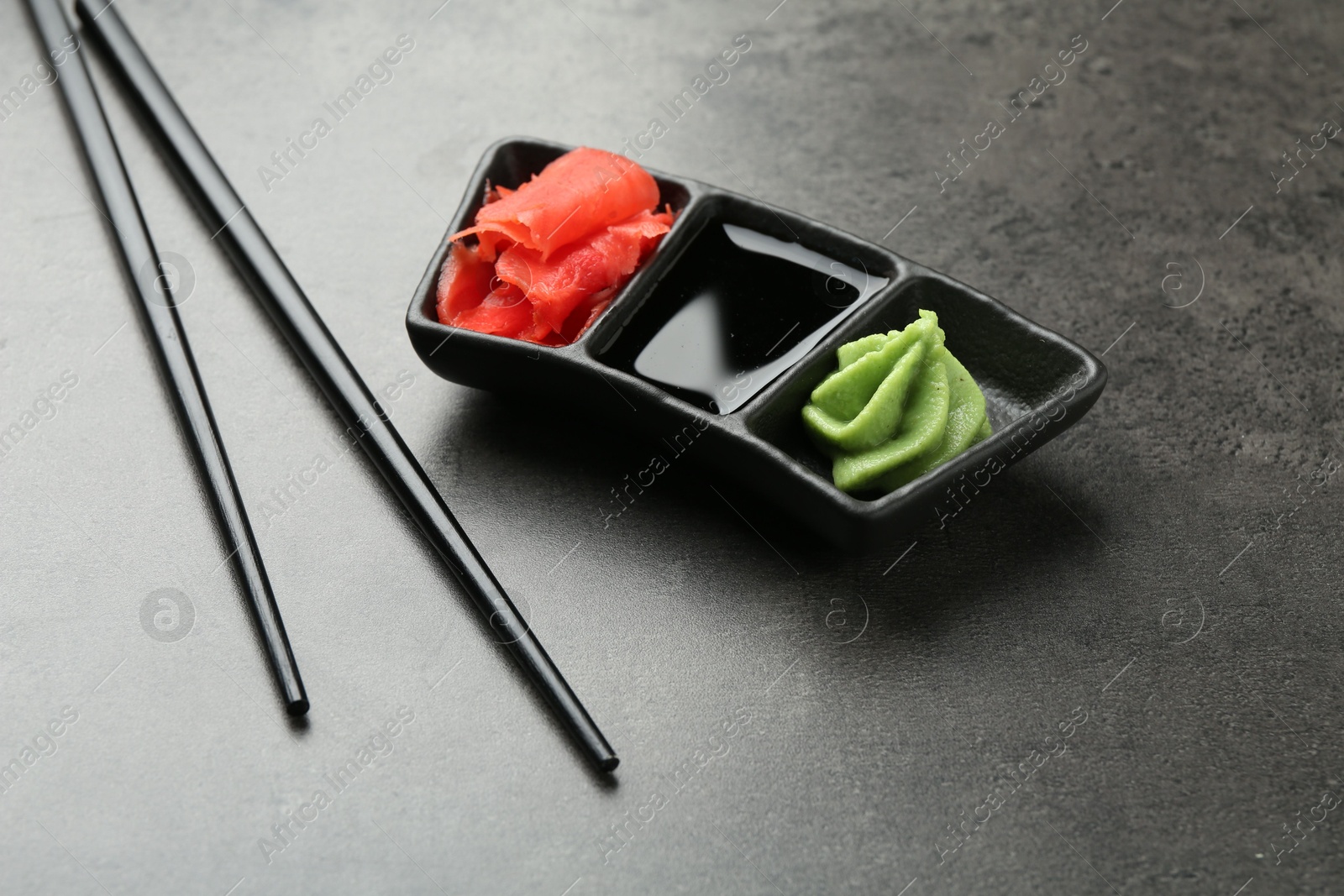 Photo of Hot wasabi paste, soy sauce, ginger and chopsticks on grey textured table, closeup