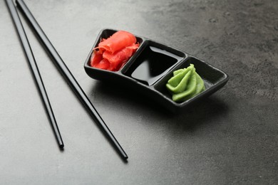 Photo of Hot wasabi paste, soy sauce, ginger and chopsticks on grey textured table, closeup