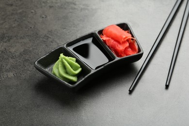 Photo of Hot wasabi paste, soy sauce, ginger and chopsticks on grey textured table, closeup