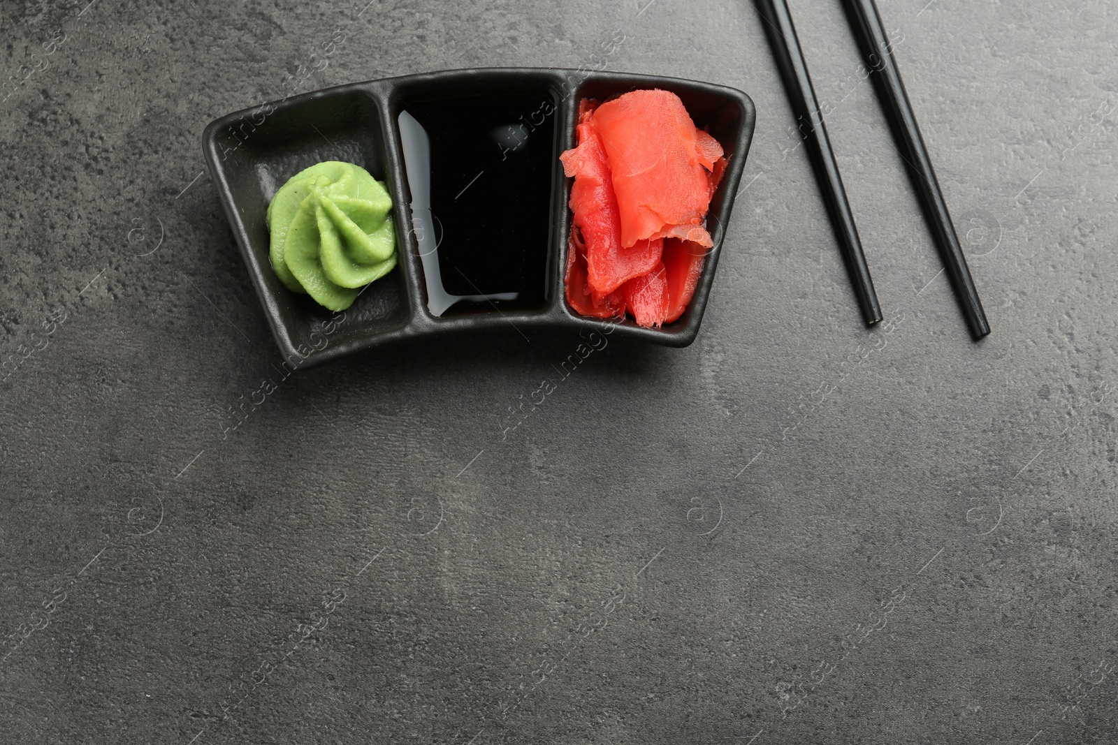 Photo of Hot wasabi paste, soy sauce, ginger and chopsticks on grey textured table, top view. Space for text