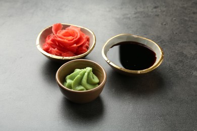 Photo of Hot wasabi paste, soy sauce and ginger on grey textured table, closeup