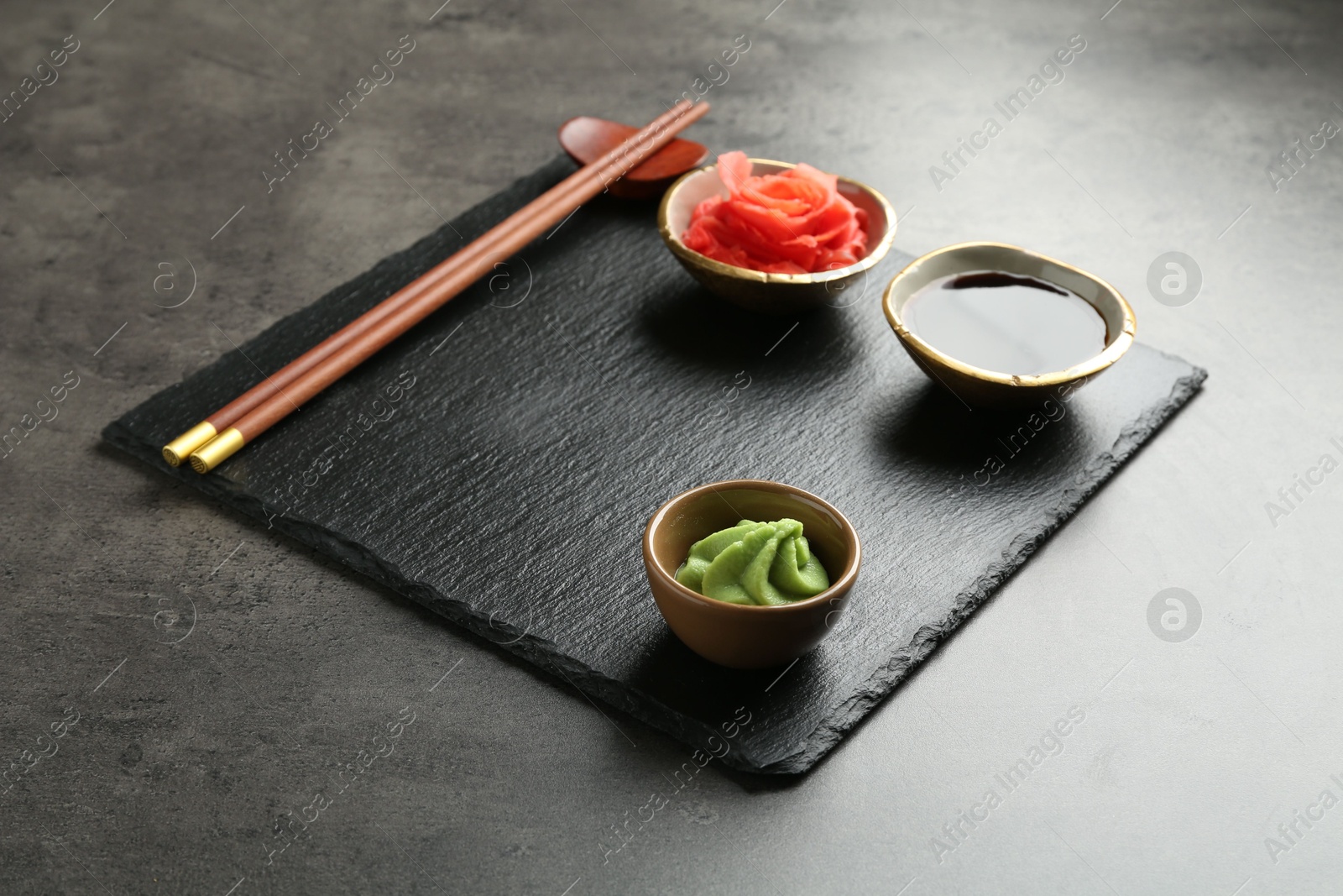 Photo of Hot wasabi paste, soy sauce, ginger and chopsticks on grey textured table, closeup