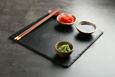 Photo of Hot wasabi paste, soy sauce, ginger and chopsticks on grey textured table, closeup