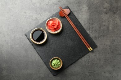 Photo of Hot wasabi paste, soy sauce, ginger and chopsticks on grey textured table, top view