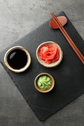 Photo of Hot wasabi paste, soy sauce, ginger and chopsticks on grey textured table, top view