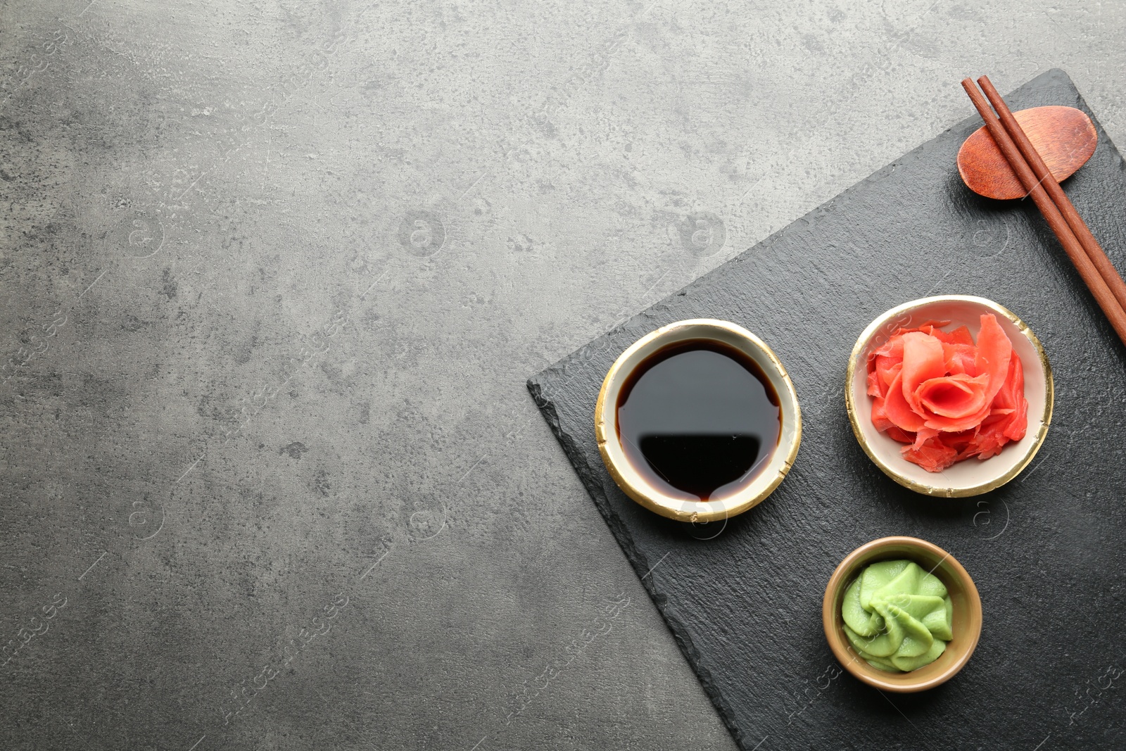 Photo of Hot wasabi paste, soy sauce and ginger on grey textured table, top view. Space for text