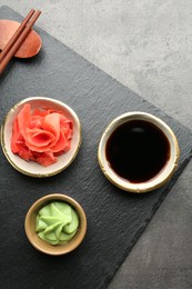 Photo of Hot wasabi paste, soy sauce and ginger on grey textured table, top view