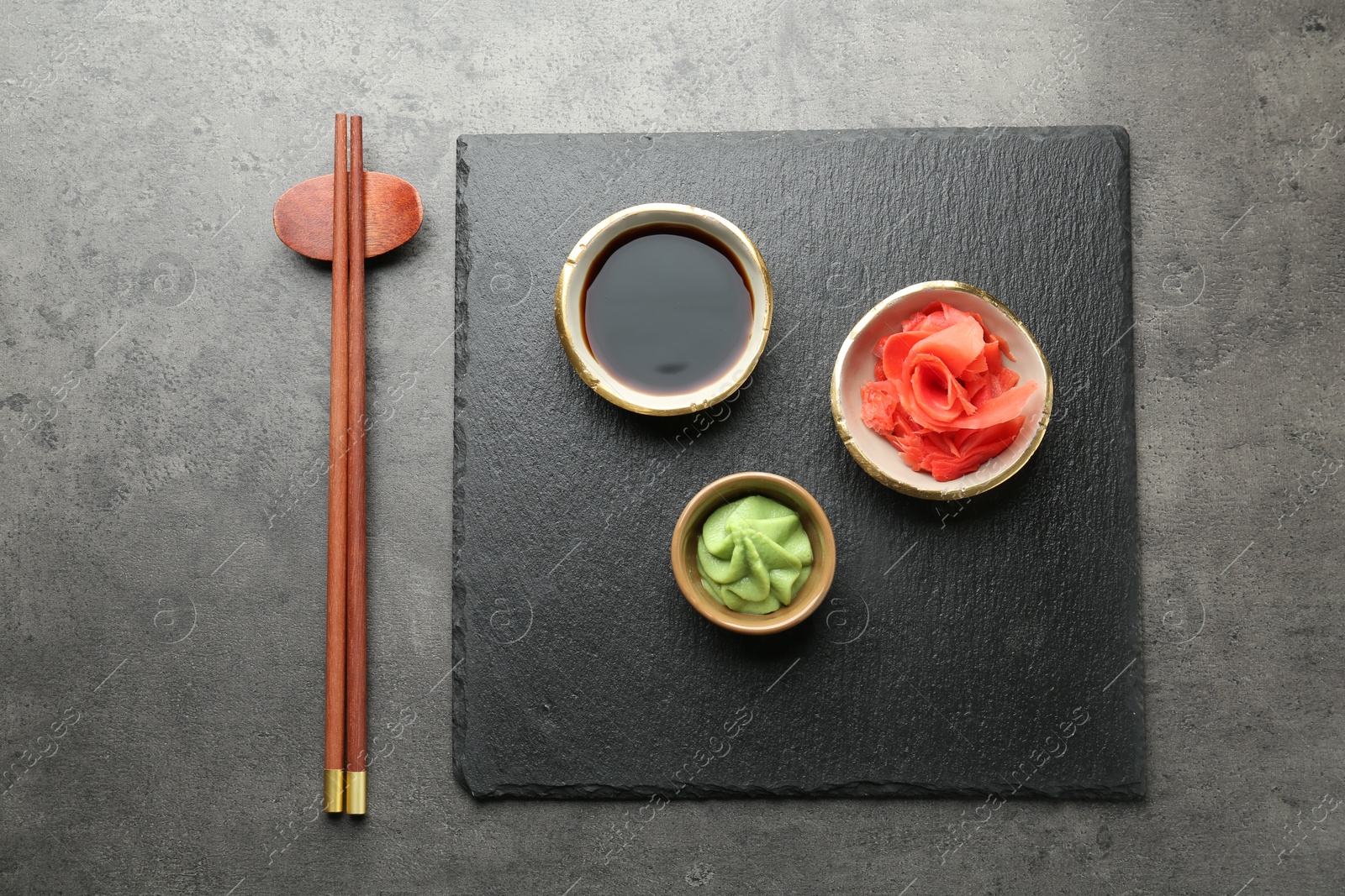 Photo of Hot wasabi paste, soy sauce, ginger and chopsticks on grey textured table, top view