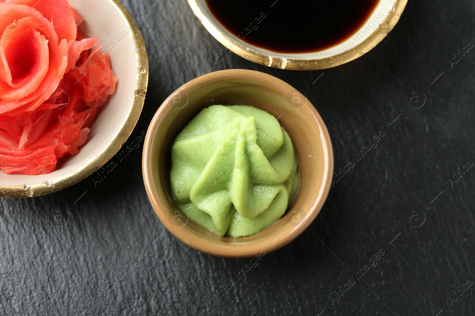 Photo of Hot wasabi paste, soy sauce and ginger on dark textured table, flat lay