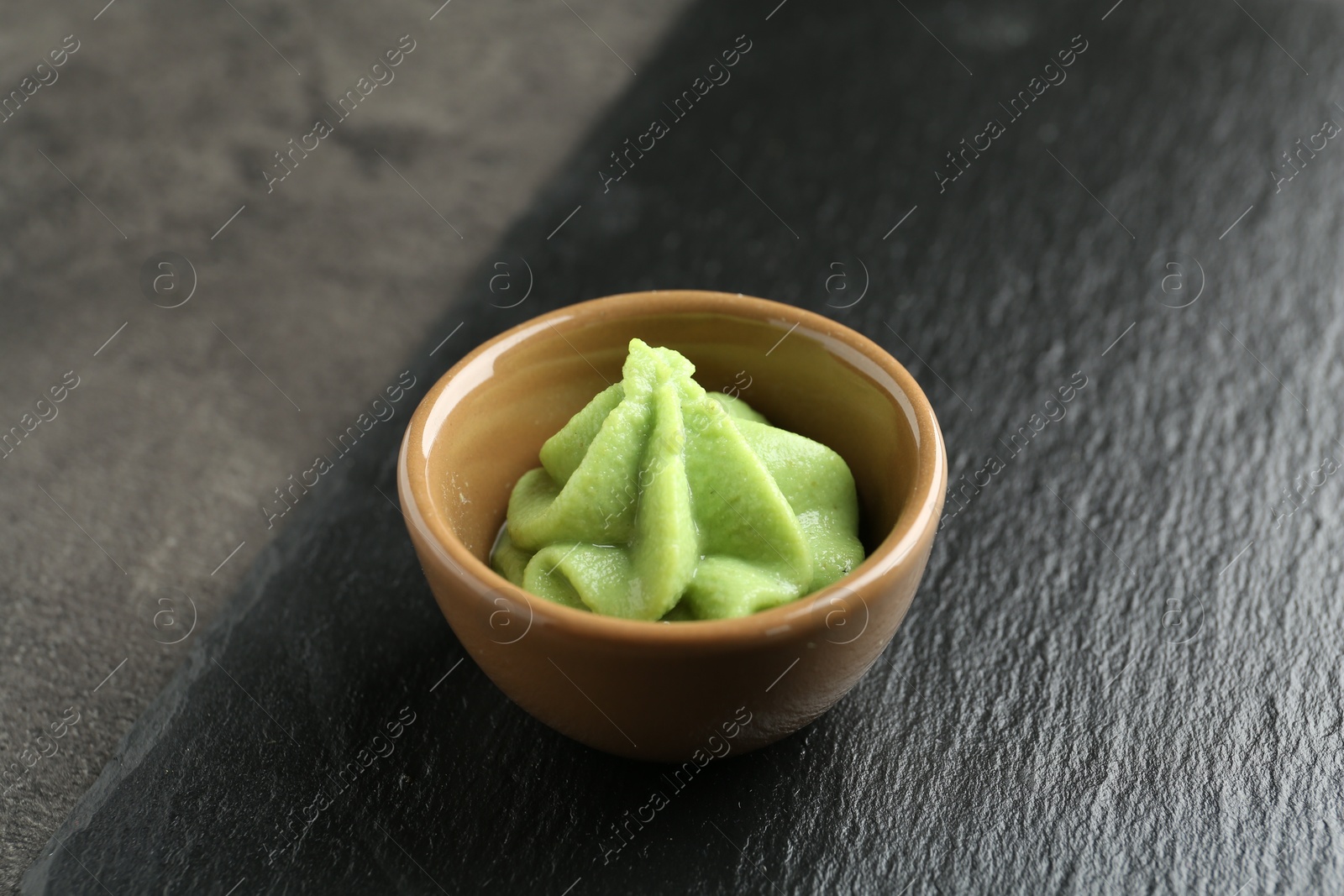 Photo of Hot wasabi paste in bowl on grey textured table, closeup