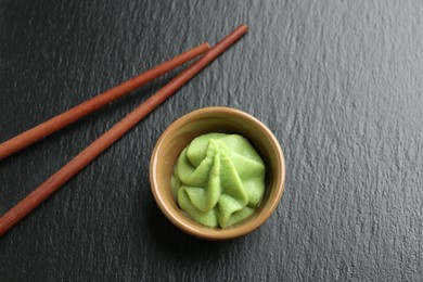 Photo of Hot wasabi paste in bowl and chopsticks on dark textured table, top view