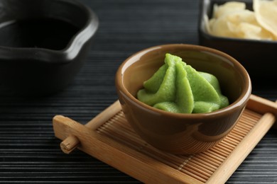 Photo of Hot wasabi paste, soy sauce and ginger on black textured table, closeup