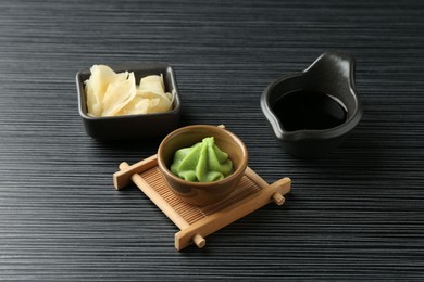 Photo of Hot wasabi paste, soy sauce and ginger on black textured table