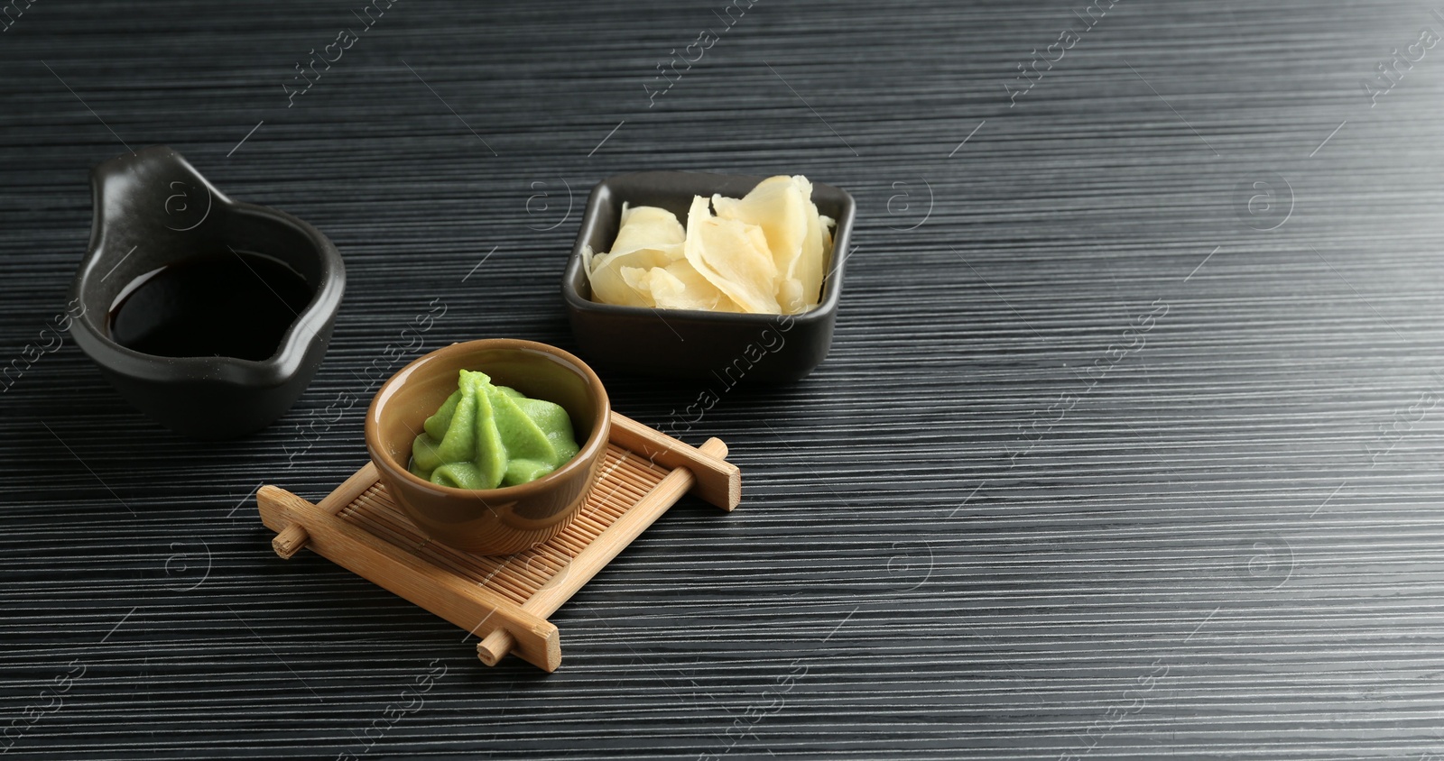 Photo of Hot wasabi paste, soy sauce and ginger on black textured table. Space for text