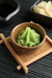 Photo of Hot wasabi paste, soy sauce and ginger on black textured table, closeup