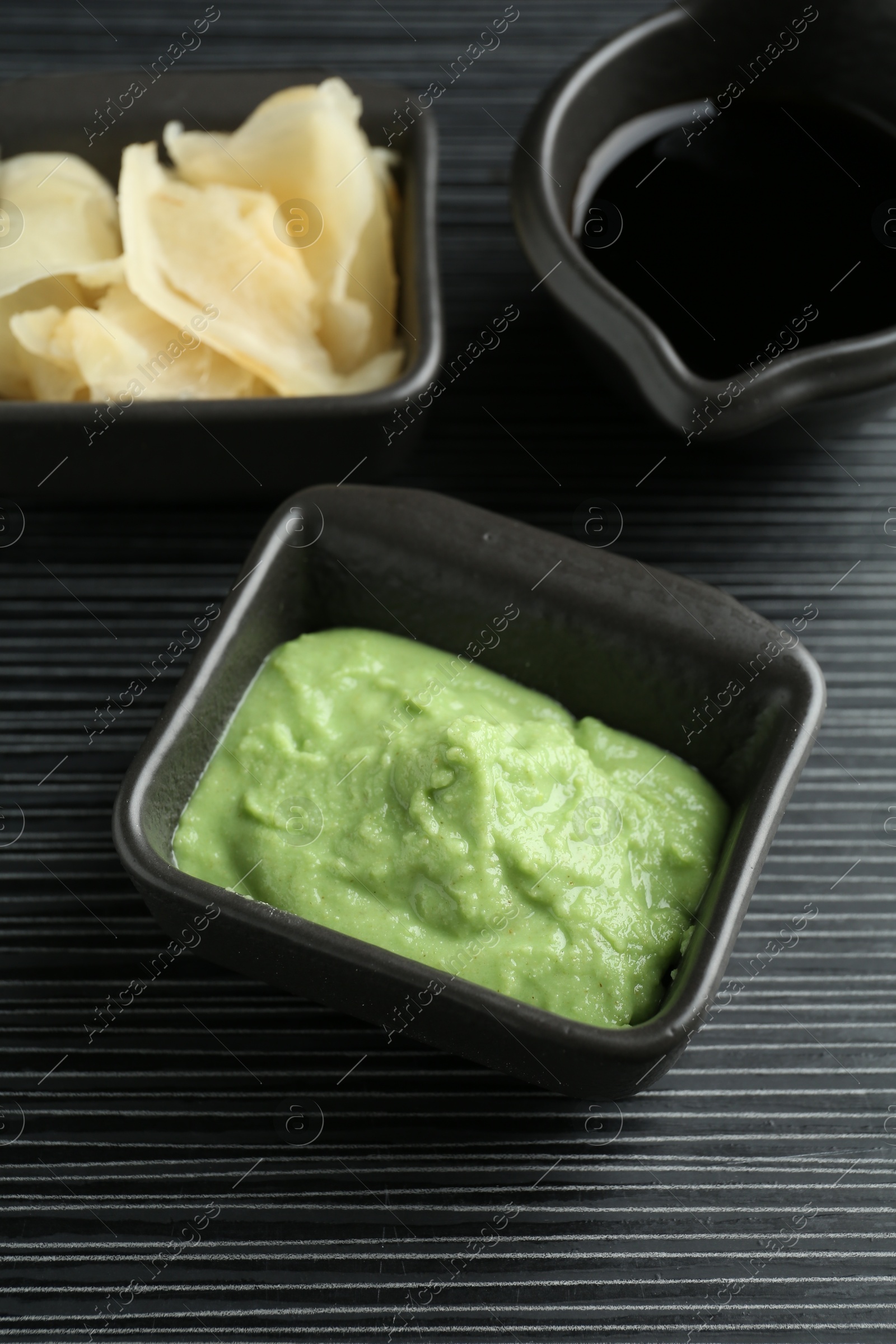 Photo of Hot wasabi paste, soy sauce and ginger on black textured table, closeup