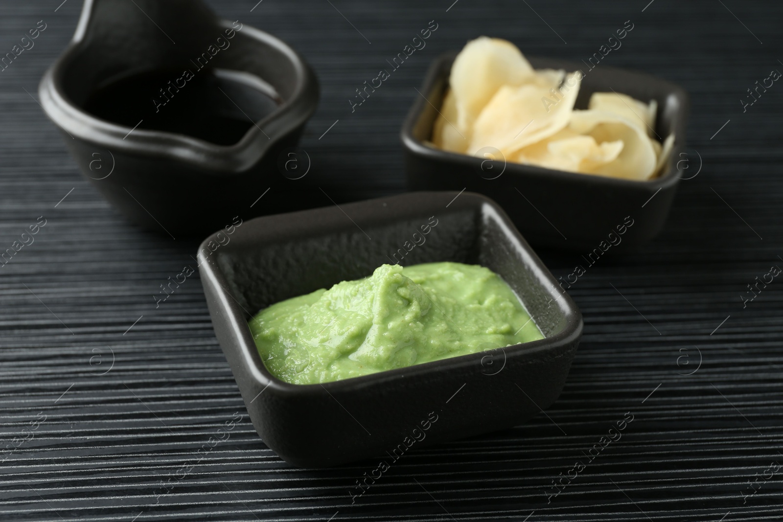 Photo of Hot wasabi paste, soy sauce and ginger on black textured table, closeup