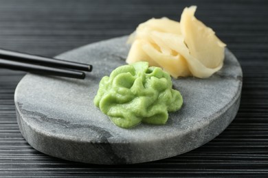 Photo of Marble board with hot wasabi paste, ginger and chopsticks on black textured table, closeup