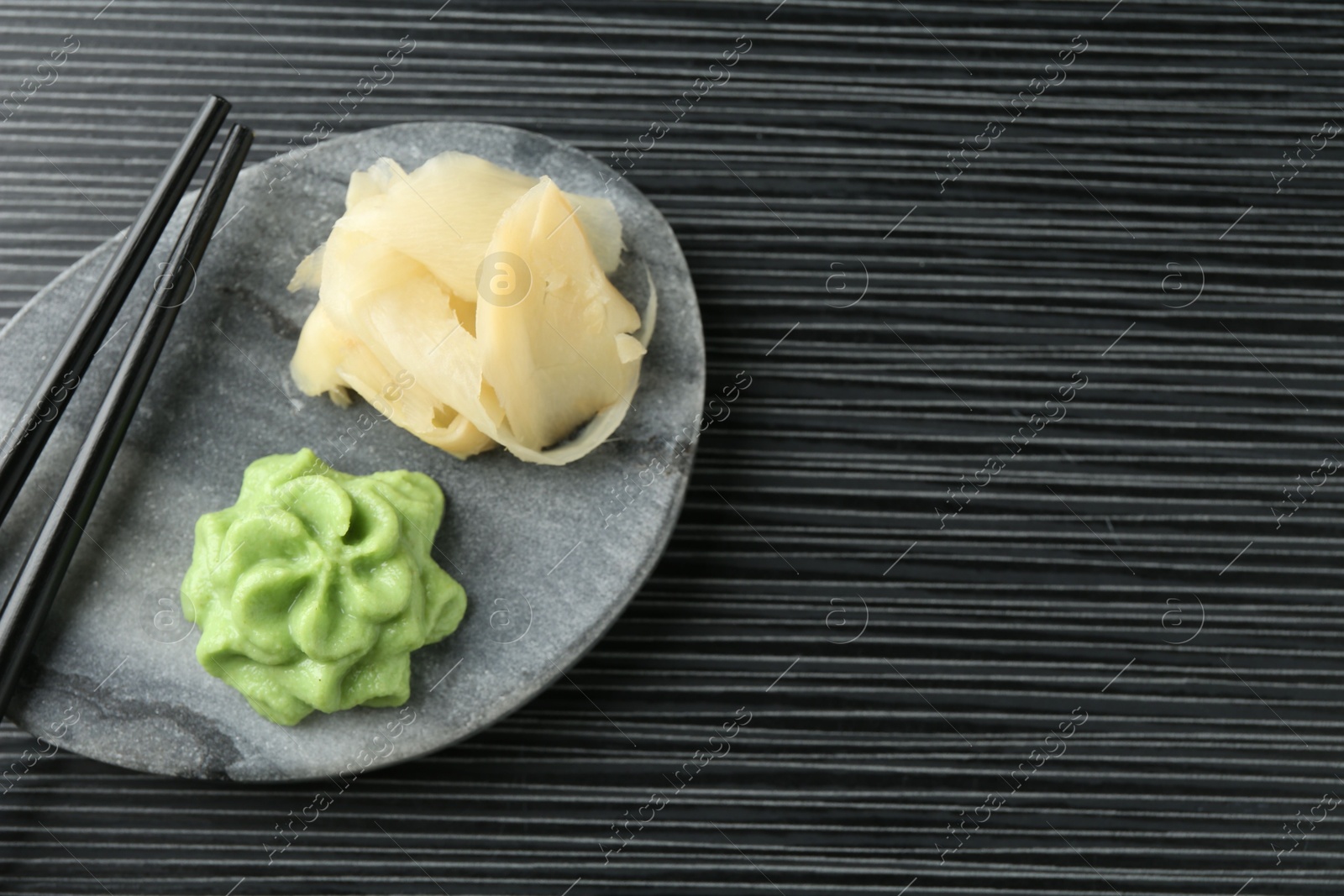 Photo of Hot wasabi paste, ginger and chopsticks on black textured table, top view. Space for text