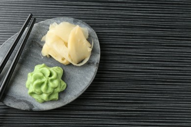 Photo of Hot wasabi paste, ginger and chopsticks on black textured table, top view. Space for text