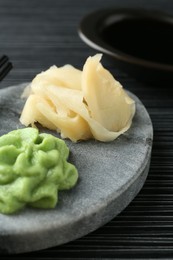 Photo of Hot wasabi paste, soy sauce and ginger on black textured table, closeup