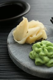 Photo of Hot wasabi paste, soy sauce and ginger on black textured table, closeup