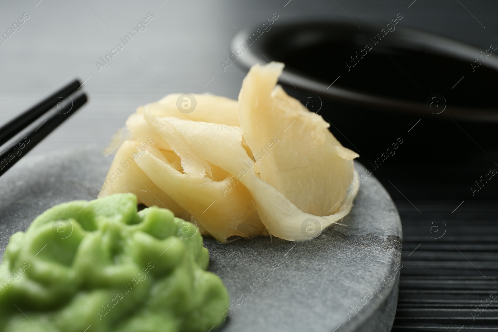 Photo of Hot wasabi paste and ginger on black textured table, closeup