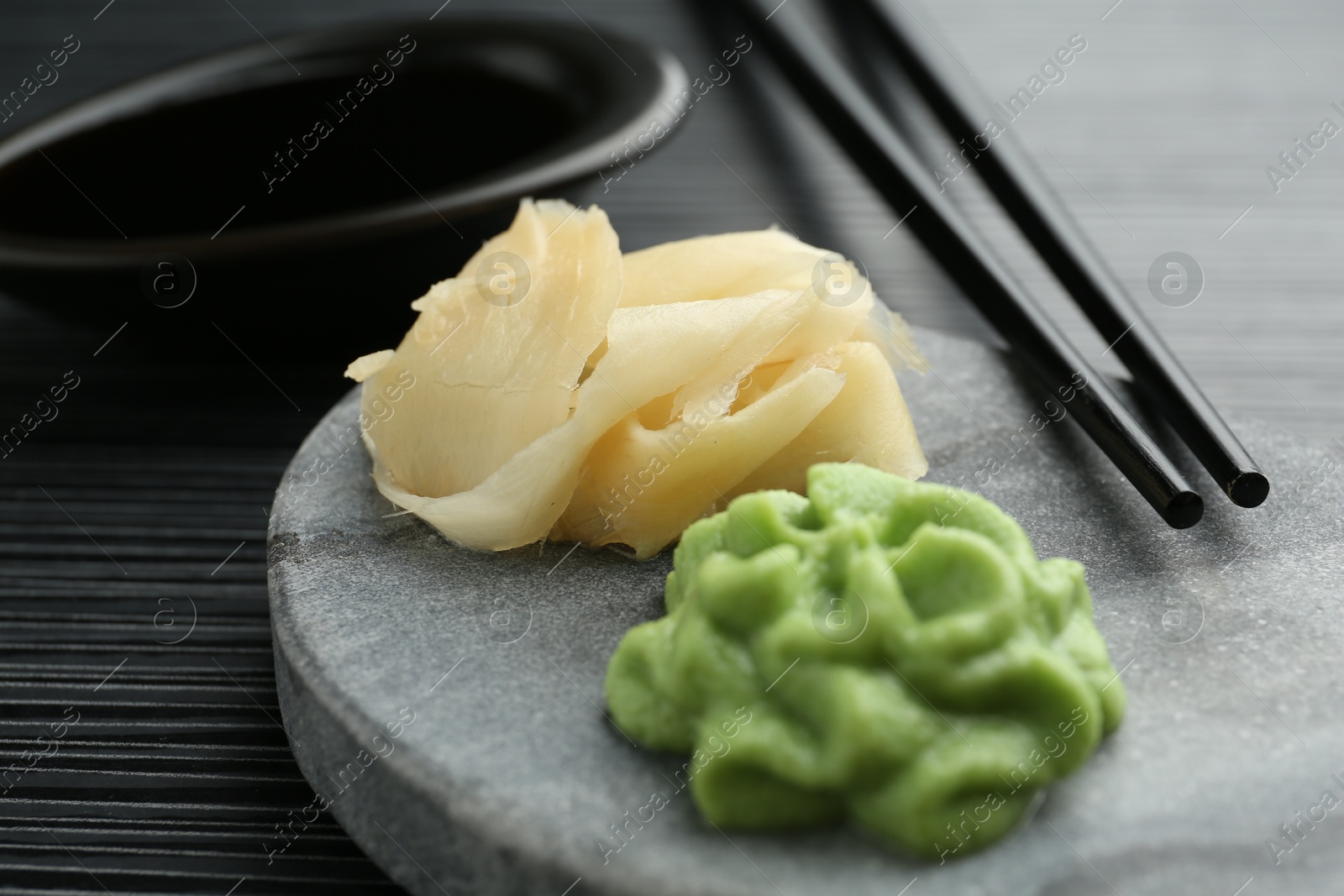 Photo of Hot wasabi paste, chopsticks and ginger on black textured table, closeup