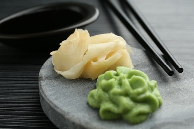 Photo of Hot wasabi paste, chopsticks and ginger on black textured table, closeup