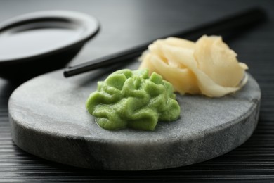 Photo of Hot wasabi paste, chopsticks and ginger on black textured table, closeup