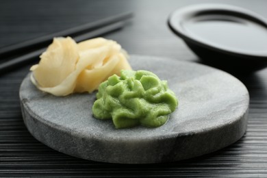 Photo of Hot wasabi paste and ginger on black textured table, closeup