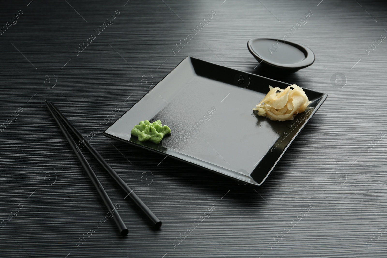 Photo of Hot wasabi paste, soy sauce, ginger and chopsticks on black textured table