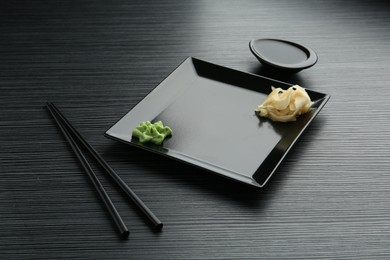 Photo of Hot wasabi paste, soy sauce, ginger and chopsticks on black textured table