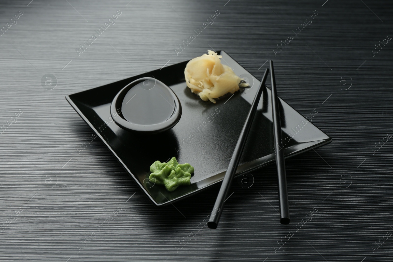 Photo of Hot wasabi paste, soy sauce, ginger and chopsticks on black textured table