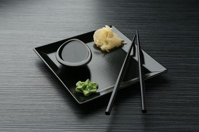 Photo of Hot wasabi paste, soy sauce, ginger and chopsticks on black textured table