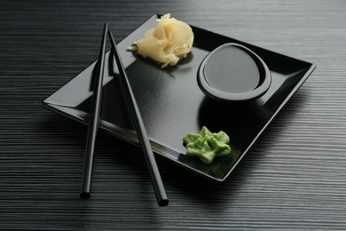 Photo of Hot wasabi paste, soy sauce, ginger and chopsticks on black textured table, closeup